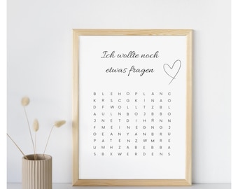 May include: A framed print with the German phrase "Ich wollte noch etwas fragen" (I still wanted to ask something) and a heart. Below the text is a word search puzzle. A beige vase with dried flowers is on the left.
