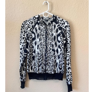 May include: A black, white, and gray leopard print zip-up hoodie with a black bottom hem and cuffs. The hoodie has a hood and a decorative embellishment down the front. The word "BETICK" is printed on the hood.