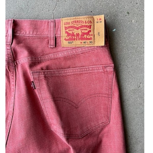 Könnte beinhalten: Nahaufnahme einer roten Levi's 501 Jeans. Die Jeans hat ein klassisches Fünf-Taschen-Design, ein rotes Levi's-Etikett und die Bundweite ist W 40 und die Länge ist L 30. Die Jeans ist ein klassischer Stil.