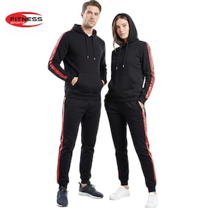 Puede incluir: Chándales deportivos negros con rayas laterales rojas. Cada chándal incluye una sudadera con capucha y pantalones a juego. El logotipo "FITNESS SPORTS" es visible en la esquina superior izquierda. Dos personas visten estos conjuntos.