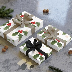 Puede incluir: Tres regalos envueltos con un diseño de acebo y bayas sobre fondo blanco. Los regalos están atados con cintas marrones y negras. La escena incluye agujas de pino, nueces y etiquetas de regalo.