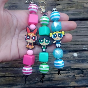 Peut inclure: Porte-clés avec les personnages des Super Nanas : Belle, Bulle et Rebelle. Chaque porte-clés est composé de perles colorées, roses, vertes, bleues et à rayures. Les porte-clés sont attachés à un fermoir argenté.
