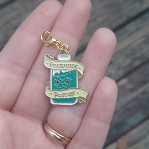 May include: A gold charm with a lobster clasp, depicting a green and white enamel potion bottle. The bottle has a cartoon face and the words "Polyjuice Potion" on a banner.