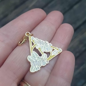 Puede incluir: Colgante dorado con diseño floral en forma triangular. El colgante tiene un contorno amarillo y está adornado con detalles florales blancos y verde claro. Incluye un pequeño cierre.