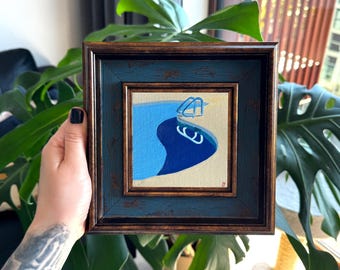 Puede incluir: Una pequeña pintura cuadrada en un marco desgastado de color azul y marrón oscuro. La obra representa una piscina estilizada con agua azul claro y azul oscuro, una plataforma beige y una escalera blanca, firmada con una marca roja.