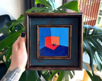 Puede incluir: Una pintura al óleo cuadrada en un marco de color bronce oscuro envejecido. La obra representa a un pequeño gato negro sentado en la esquina de una habitación con paredes de color azul vibrante y un suelo rojo brillante, creando un contraste.