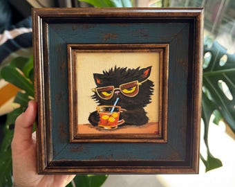Puede incluir: Pintura enmarcada de un gato negro con gafas de sol bebiendo una bebida con una pajita. La pintura tiene un marco azul oscuro y marrón. El gato está representado con una bebida en un vaso.