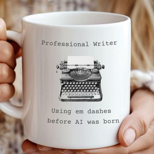 Könnte beinhalten: Weiße Keramiktasse mit dem Text "Professional Writer" und "Using em dashes before AI was born." Die Tasse zeigt eine Schwarz-Weiß-Illustration einer alten Schreibmaschine.