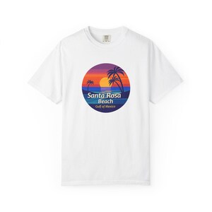 May include: White t-shirt with a circular graphic depicting a sunset over Santa Rosa Beach, Gulf of Mexico. The design includes palm trees, a colourful sky, and the text "Santa Rosa Beach". The shirt is made of a soft, comfortable material.