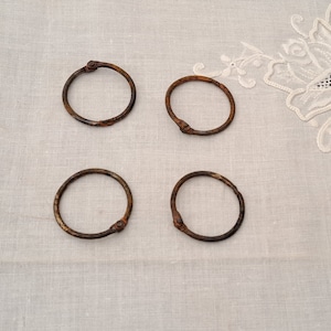 May include: Four rusty metal rings, possibly binder rings, on a white fabric background.