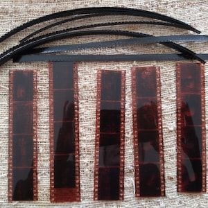 Puede incluir: Cinco tiras de película de 35 mm, cada una con varios fotogramas, se colocan sobre una superficie de tela beige. La película está expuesta y muestra un color marrón rojizo.