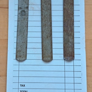 May include: A white check with a blue grid pattern. The check has a check number of "4437-3". There are three rusty metal clips on the check.