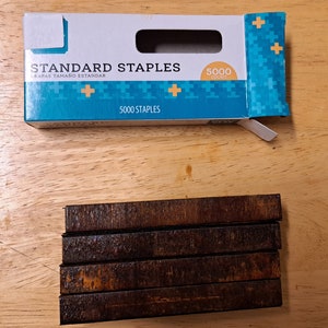 May include: A box of 5000 standard staples. The box is blue and white with a plus sign pattern. The staples are in a brown metal strip.