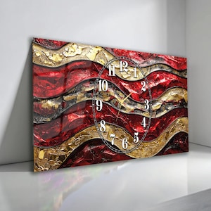 May include: A rectangular wall clock featuring an abstract design of flowing, layered waves in deep red, black, and metallic gold. The clock face is overlaid with a circular black frame containing white Arabic numerals and thin gold clock hands.