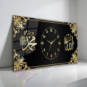 Può includere: Un orologio da parete rettangolare nero con dettagli dorati e calligrafia araba. Il quadrante dell'orologio è nero con lancette e numeri dorati. Decorazioni dorate adornano gli angoli e la cornice. L'orologio presenta i nomi di Allah e Maometto.