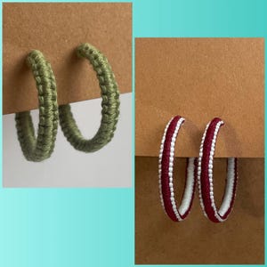 May include: Two pairs of handmade hoop earrings. One pair is olive green, and the other is burgundy with white stripes. The earrings are displayed on brown card, showcasing the woven texture of the jewellery.