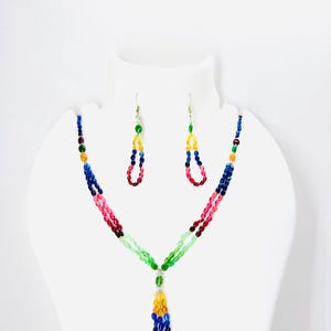Könnte beinhalten: Ein farbenfrohes Perlenkette und Ohrring-Set. Die Halskette hat Stränge aus roten, rosa, grünen, gelben und blauen Perlen. Die Ohrringe haben ein ähnliches Design, mit einer Schlaufe aus bunten Perlen. Der Schmuck wird auf einer weißen Schaufensterpuppe präsentiert.