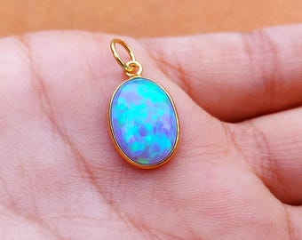 May include: A gold pendant with an oval-shaped opal. The opal has a vibrant display of blue and green colors. The pendant is held in a hand, showcasing the jewelry's design and color.