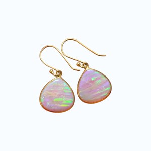 Può includere: Un paio di orecchini a goccia con pietre di opale iridescenti incastonate in metallo color oro. Gli opali mostrano un mix di tonalità rosa, bianche e verdi. Gli orecchini hanno un semplice design a gancio.