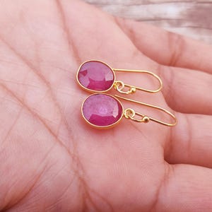 Peut inclure: Une paire de boucles d'oreilles pendantes dorées avec des pierres précieuses ovales rose foncé. Les boucles d'oreilles sont serties dans une lunette dorée et ont une fermeture à crochet simple. Les pierres précieuses sont d'une couleur vive et saturée.