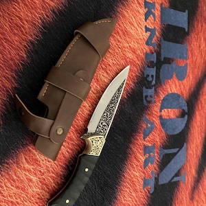 May include: A decorative knife with a silver blade and ornate gold detailing on the handle, accompanied by a brown leather sheath. The handle is black with gold accents. The text "IRON KNIFE ART" is visible in the background.