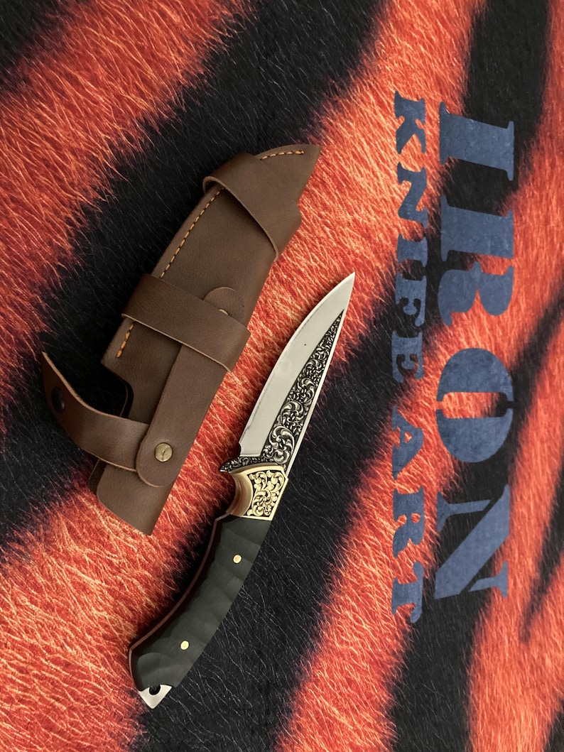 May include: A decorative knife with a silver blade and ornate gold detailing on the handle, accompanied by a brown leather sheath. The handle is black with gold accents. The text "IRON KNIFE ART" is visible in the background.