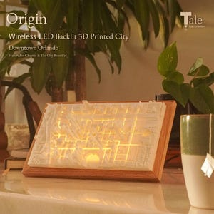 May include: A wireless LED backlit 3D printed city, featuring Downtown Orlando. The illuminated cityscape is encased in a wooden frame. The text "Origin" and "Tale Print Company" are visible.