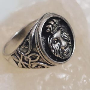 Könnte beinhalten: Silberfarbener Ring mit einem detaillierten Löwenkopf mit Krone in einem kreisförmigen Rahmen. Das Band des Rings weist ein aufwendiges Muster auf. Der Ring ist aus Metall gefertigt und für den täglichen Gebrauch geeignet.