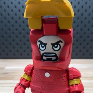 K&ouml;nnte beinhalten: Eine rot-gelbe Iron Man-Figur mit einem blockartigen Design. Die Figur hat einen Helm mit einem Gesicht und eine gelbe Struktur oben. Sie hat einen wei&szlig;en Kreis auf der Brust und gelbe Akzente an Armen und Beinen.
