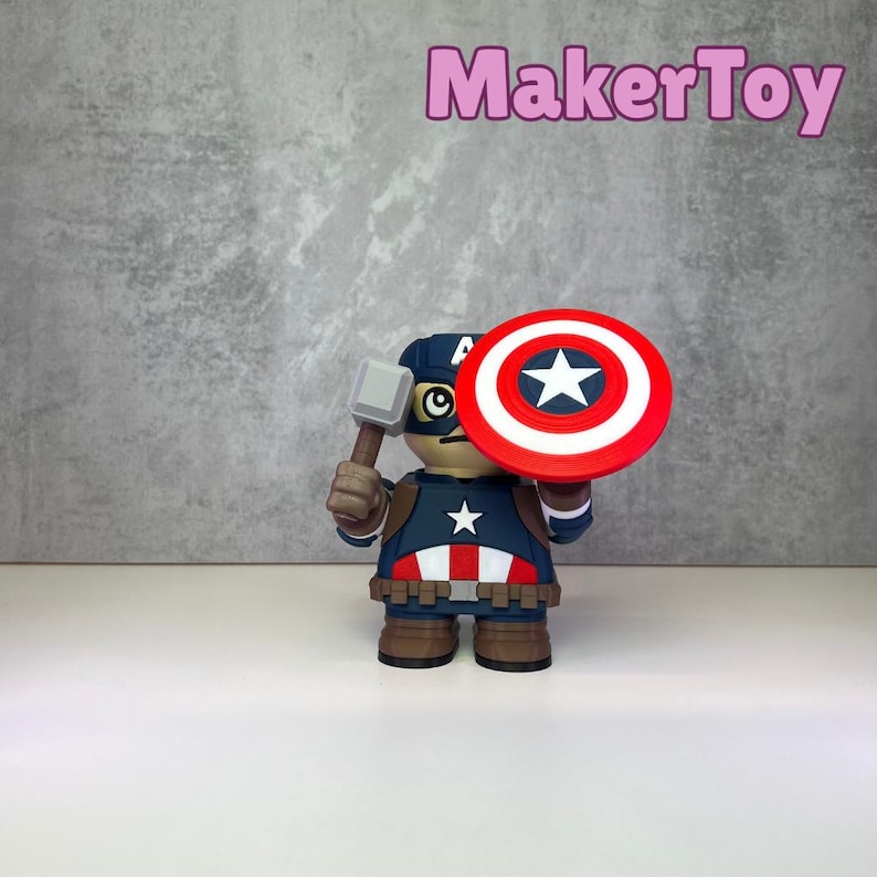 May include: A Captain America figurine holding a hammer and shield. The shield is red, white, and blue with a white star. The figurine is wearing a blue and red costume with a white star on the chest. The text "MakerToy" is in pink.