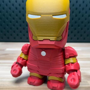 K&ouml;nnte beinhalten: Eine rot-goldene Iron Man-Figur. Die Figur hat ein blockartiges Design mit einem goldenen Helm und roter R&uuml;stung. Die Figur hat einen kleinen wei&szlig;en Kreis auf der Brust und gelbe Akzente an den Gelenken.