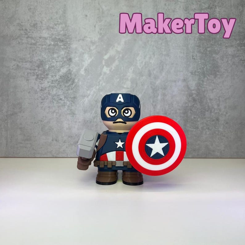 May include: A Captain America figurine with a red, white, and blue shield and a hammer. The figurine is wearing a blue helmet with a white "A" and a blue and white star on the chest. The text "MakerToy" is in pink.