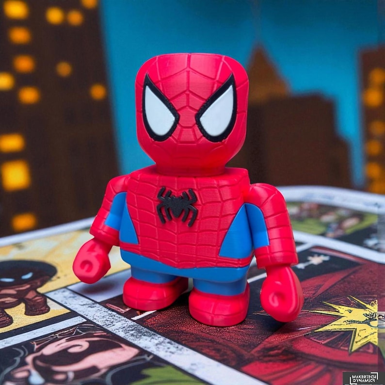 May include: A red and blue Spider-Man figurine with a black spider emblem on the chest. The figure has white eye details and is posed on a comic book page. The figure is a stylized, blocky design.