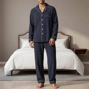 Può includere: Pigiama blu navy con texture a coste, profili bianchi e camicia con bottoni. La camicia a maniche lunghe ha una tasca sul petto. I pantaloni del pigiama hanno una vestibilità ampia. Il set è esposto in una camera da letto.