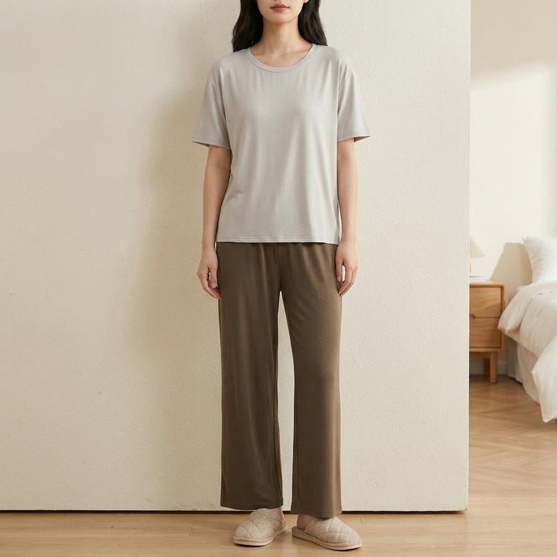 May include: A light gray short-sleeved crew neck t-shirt paired with solid dark brown wide-leg lounge pants. The outfit is completed with a pair of beige quilted slip-on slippers, creating a simple and coordinated two-piece loungewear set.