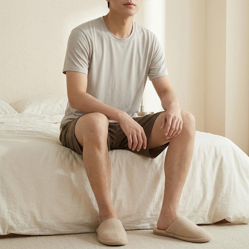 May include: A light gray short-sleeved crew neck t-shirt paired with dark olive green shorts and beige slip-on slippers. The clothing set features a simple design with solid colors, providing a neutral and understated appearance for casual loungewear.