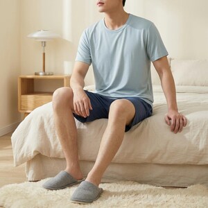 May include: A light blue short-sleeved crew neck t-shirt paired with dark blue shorts and grey slip-on slippers. The t-shirt features a simple design with a round neckline, while the shorts are knee-length and the slippers have a soft texture.