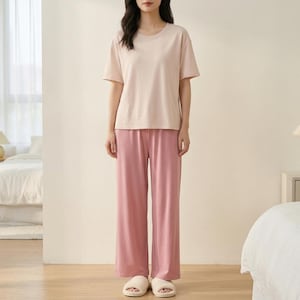 May include: A short-sleeved crew neck t-shirt in a light beige color paired with loose-fitting, wide-leg trousers in a solid dusty rose pink color. The outfit is completed with a pair of light-colored, open-toed slip-on house slippers.