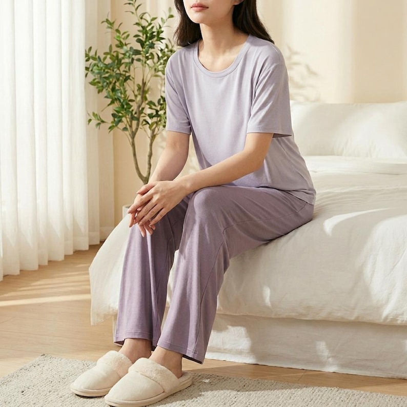 May include: A light purple short-sleeved t-shirt and matching long pants lounge set. The top features a round neckline and short sleeves, while the pants have a straight-leg cut. The set is made of a solid-colored, smooth fabric in a soft lavender hue.
