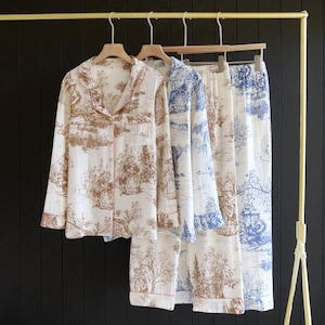 Peut inclure: Deux ensembles de pyjamas suspendus à un portant doré. L'un est blanc avec un imprimé toile de Jouy marron, l'autre est blanc avec un imprimé toile de Jouy bleu. Les deux ensembles comprennent une chemise boutonnée et un pantalon assorti.