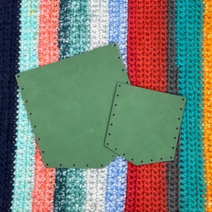 May include: Two olive green, geometric shapes with evenly spaced holes along the edges, resting on a colorful, striped, crocheted background. The shapes are a larger rectangle and a smaller square, possibly for crafting.