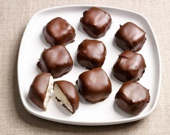 May include: A white plate with nine chocolate-covered treats. The treats are square and have a white filling. Some of the treats are cut in half, revealing the white filling.