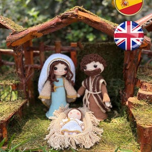 May include: A handcrafted nativity scene featuring crocheted figures of Mary, Joseph, and baby Jesus in a manger. The figures are dressed in blue, brown, and white, set within a rustic wooden stable with green moss.