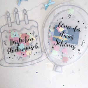 Könnte beinhalten: Zwei transparente Karten, eine kuchenförmige mit der Aufschrift "Herzlichen Glückwunsch", die andere ballonförmig mit "Gönn dir etwas Schönes". Beide sind mit Konfetti gefüllt und mit kleinen blauen Schleifen verziert.