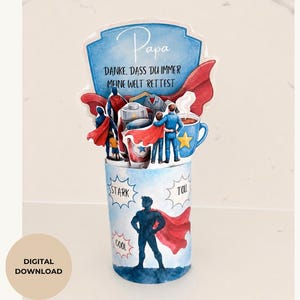 May include: A blue and white superhero-themed card with the word "Papa" and German text. The card features illustrations of superheroes, a coffee cup, and a red cape. The words "Stark", "Cool", and "Toll" are also visible.