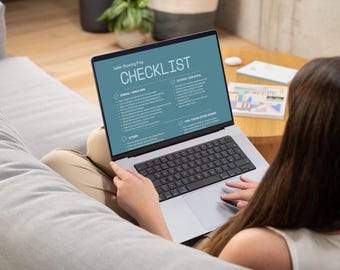 May include: A laptop displaying a "Seller Showing Prep CHECKLIST" is held by a person. The screen shows a teal background with white text, listing items for preparing a home for sale. The laptop is open on a person's lap, with a keyboard visible.