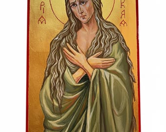 May include: A rectangular religious icon painting on a gold background featuring a figure with long wavy hair, wearing a draped olive green garment. The figure has arms crossed over the chest. Cyrillic text is inscribed on both sides of the head.