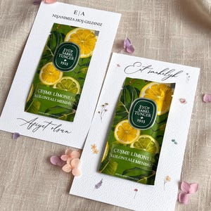 May include: Two white cards with text and a lemon-themed design. Each card features a green label with lemon slices and the text "EYÜP SABRI TUNCER 1923" and "ÇEŞME LİMONU KOLONYALI MENDİL". The cards are decorated with small flowers.