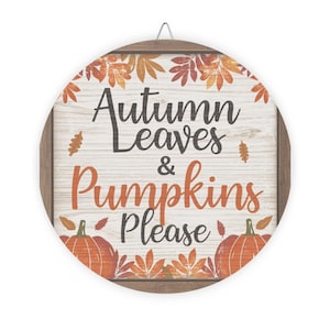 May include: Round wooden sign with the text "Autumn Leaves & Pumpkins Please". The sign features orange pumpkins and fall leaves. The background is a light wood grain pattern, and the frame is brown.