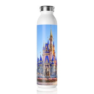 May include: A white cylindrical water bottle featuring a full-color photographic print of a pink and blue castle with tall spires and a statue in the foreground. The bottle has a metallic silver screw-top lid and a smooth, glossy finish.